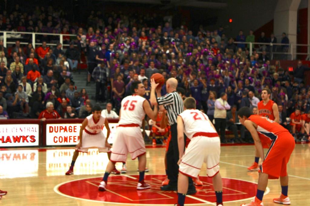 Naperville Central and Naperville North boys basketball teams meet at center court for tip off awaiting the start of the game. 