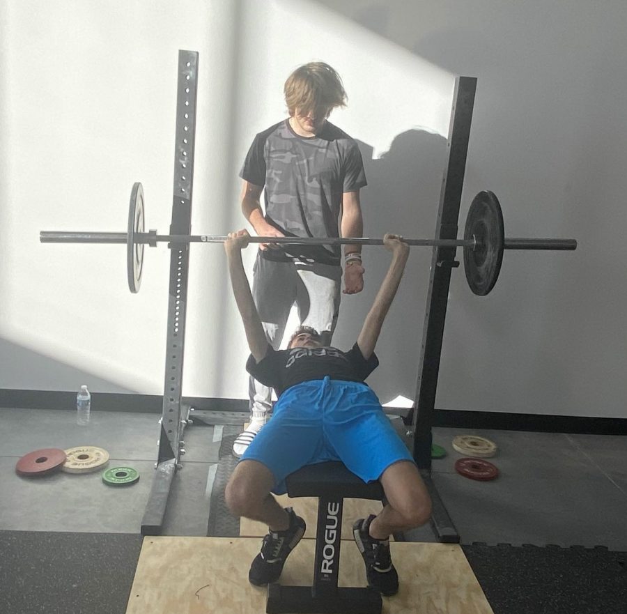 Naperville Central freshman Maverick Ohle (standing) coaches fellow Central freshman Tarek Hassabo on performing a bench press at The PowerHouse, Ohle’s Olympic gym located at 505 S Weber St.