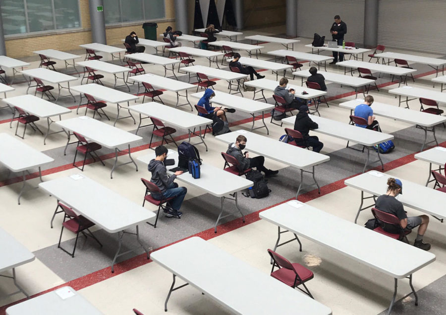 Masked hybrid learning students sit socially distanced in the cafeteria during free periods.