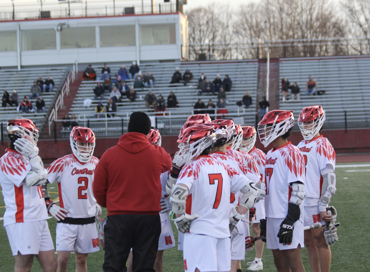 Naperville Central players huddle around head coach Blake Zinn during a timeout in their home opener against Kaneland on March 24.